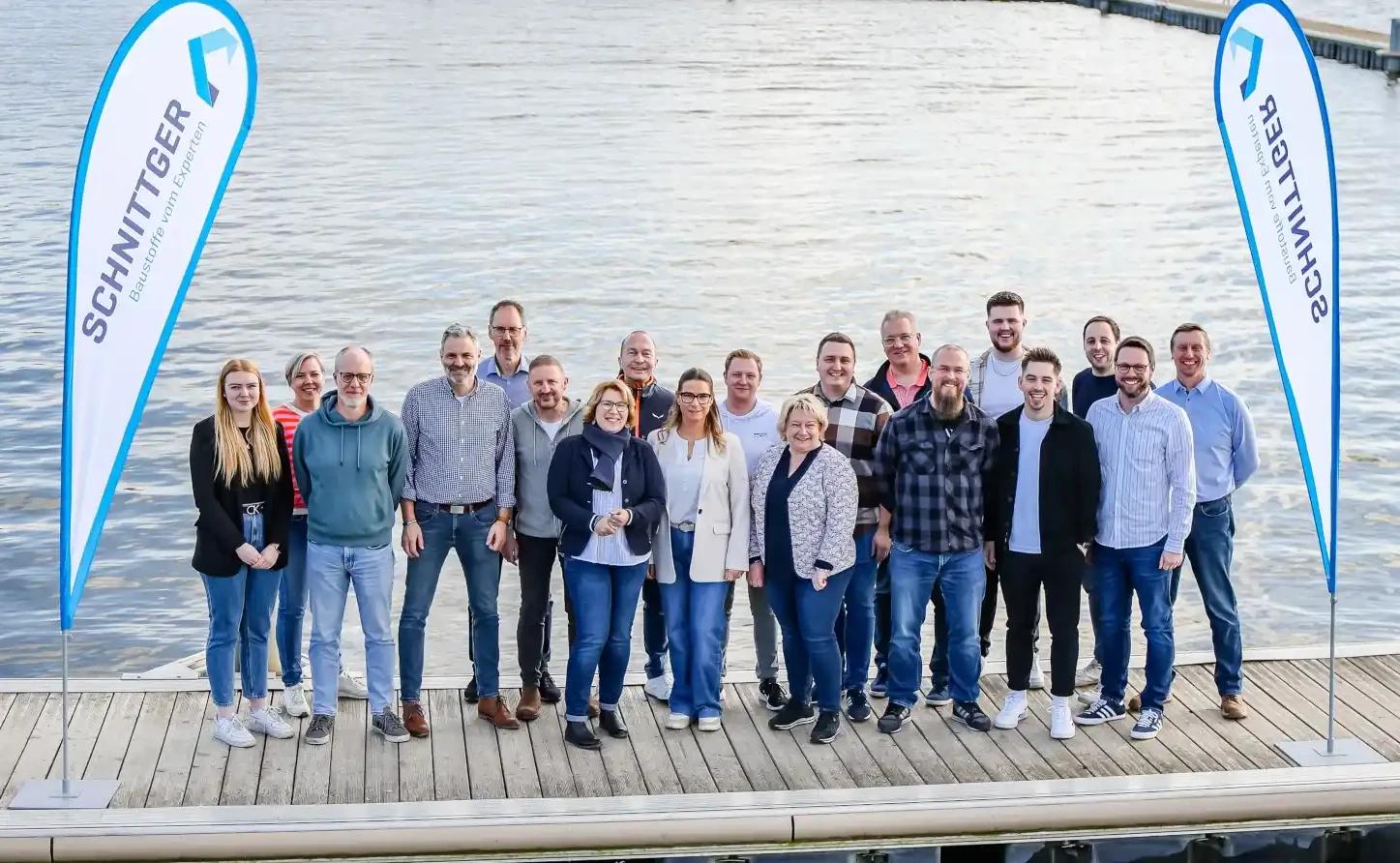 Gruppenfoto vom Schwitter-Team am Wasser, zwischen zwei Firmenfahnen am Steg
